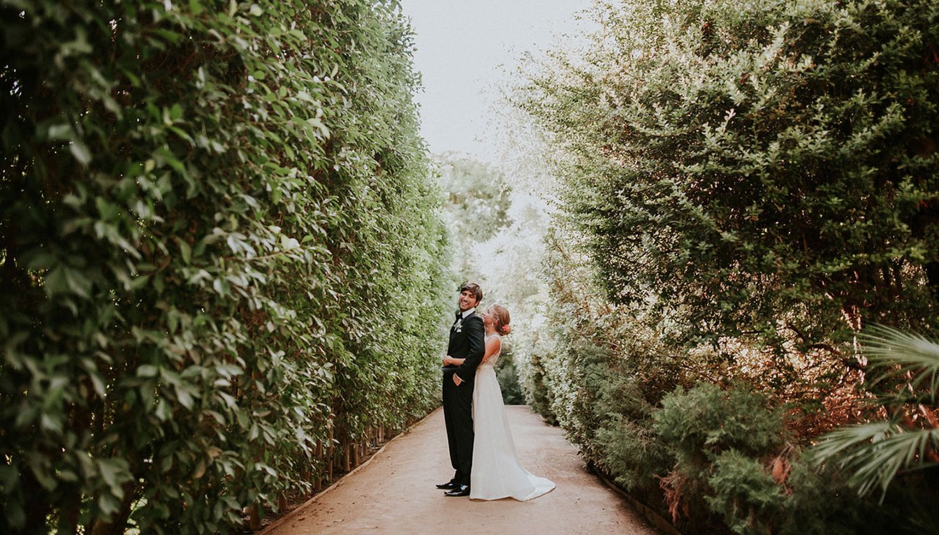 A couple stands on a pathway surrounded by trees.