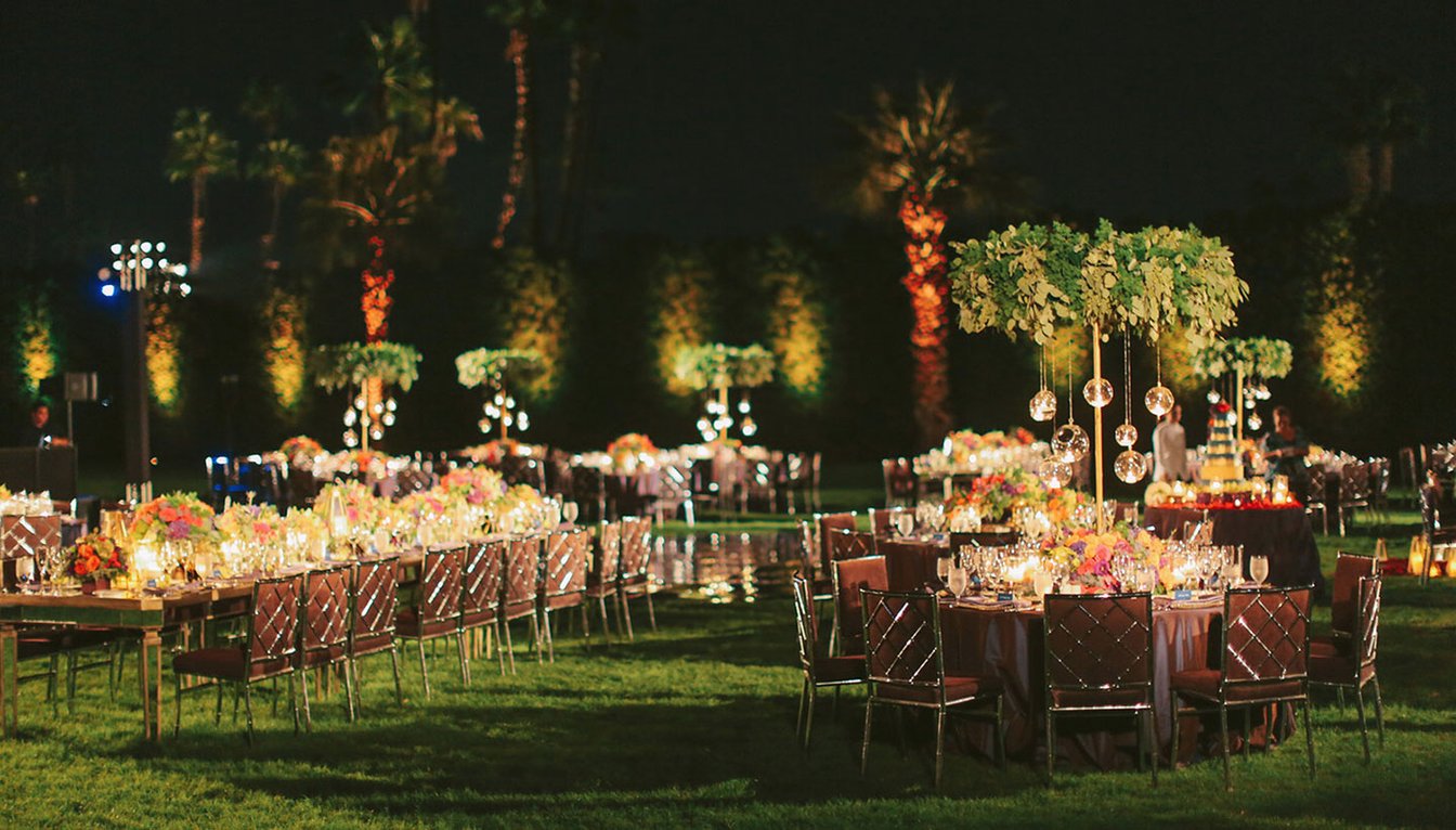 A nighttime outdoor event space with tables, chairs, flowers, and lights set up for a formal event.