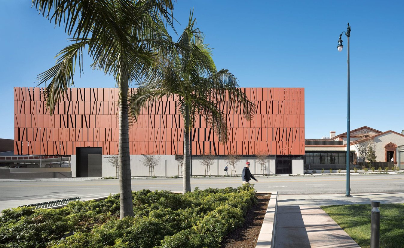 A modern building with a red facade and a palm tree in front of it.