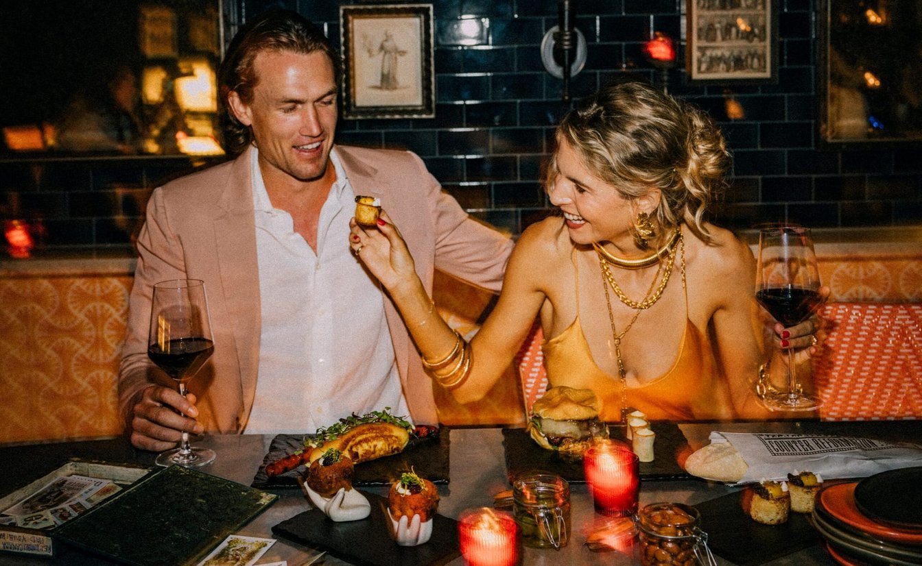A man and woman in a booth, enjoying a meal and wine.