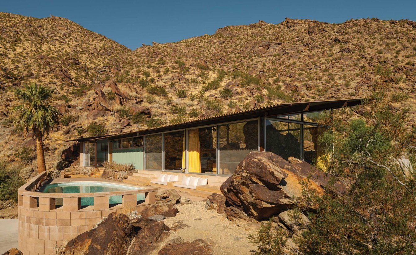 A modern building with large windows and a pool in the desert.