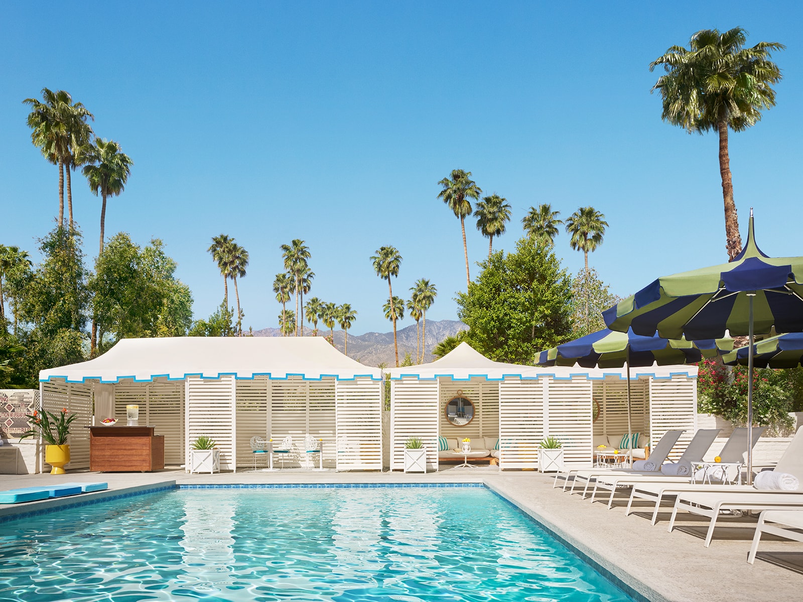 A swimming pool with a mountain view, lounge chairs, and umbrellas.