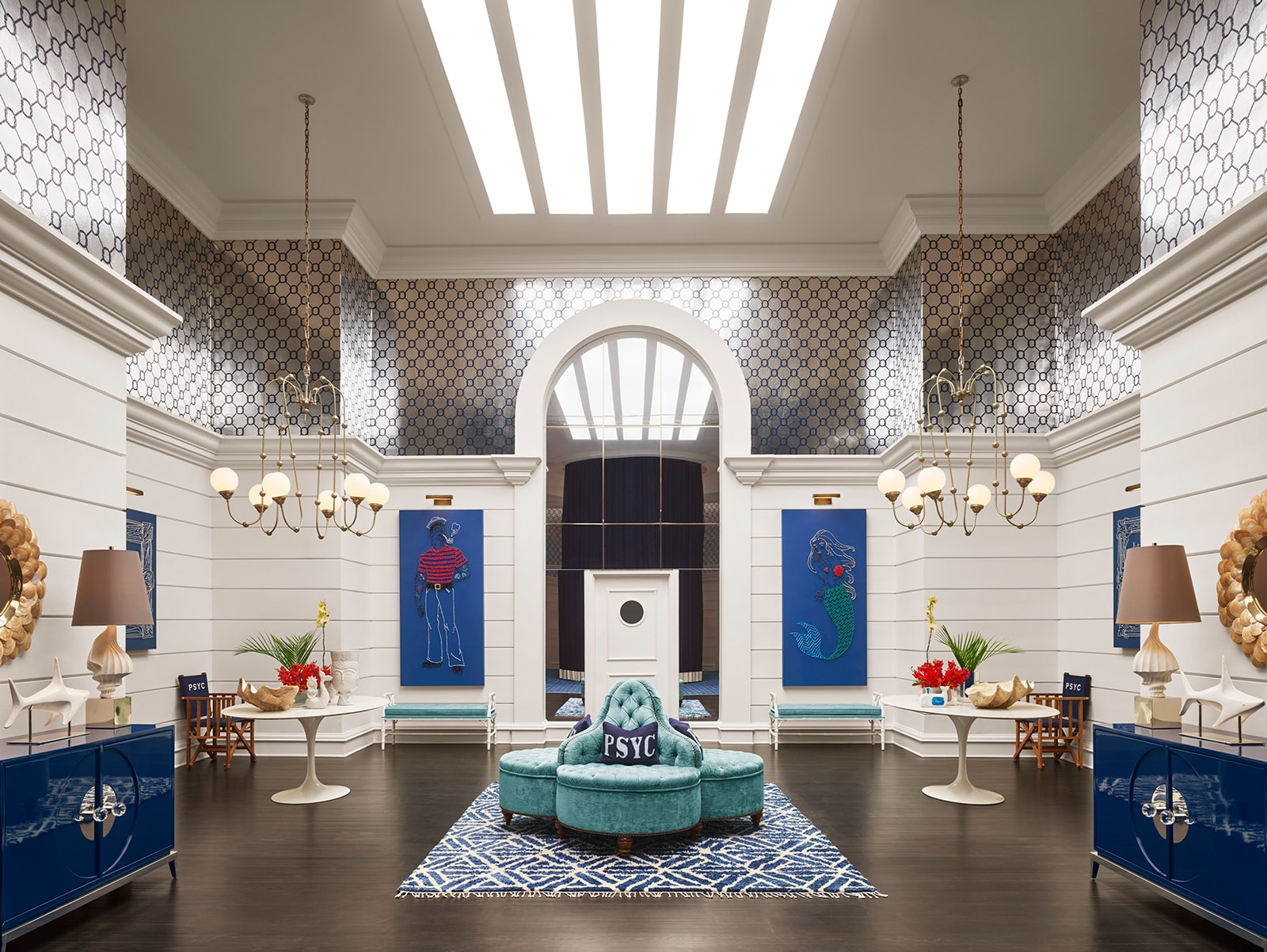 A large, bright lobby with a high ceiling, featuring a teal sofa, chandeliers, and artwork.
