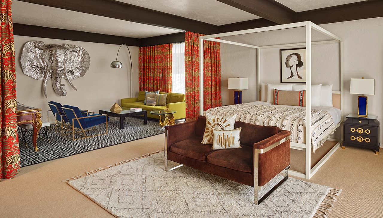 A luxurious hotel room with a four-poster bed, sitting area, and decorative art.