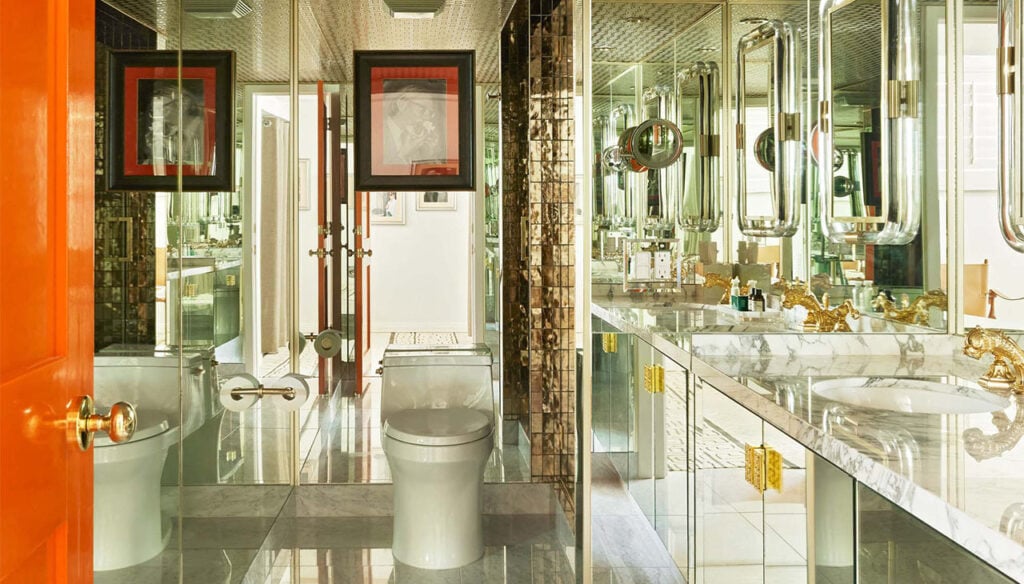 A luxurious bathroom with a double vanity, two sinks, and a toilet, featuring gold faucets, a marble countertop, and a large mirror.