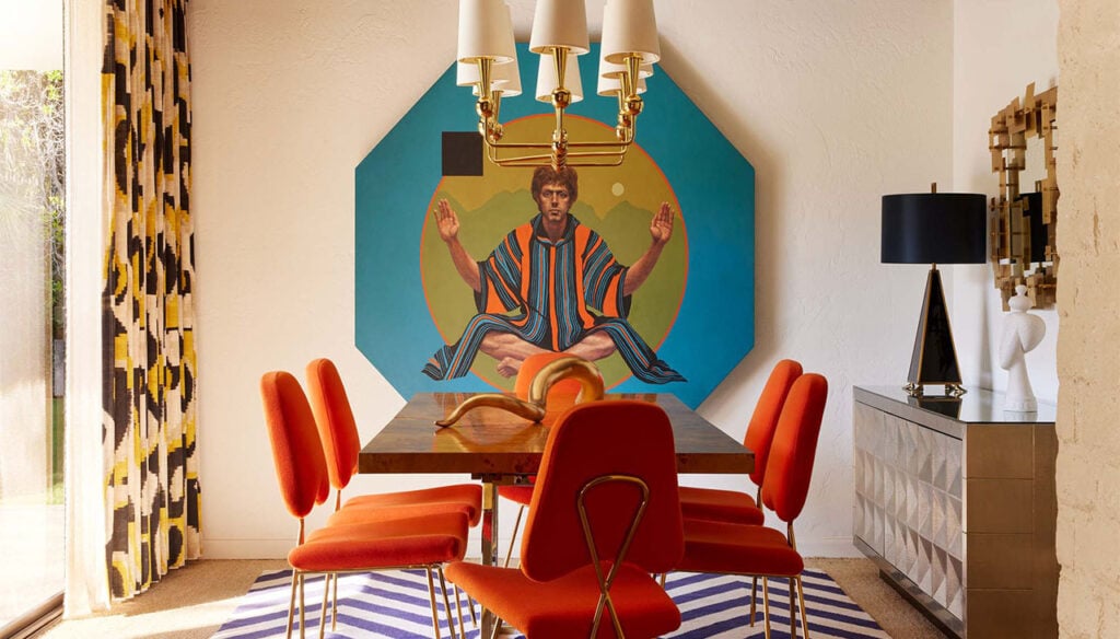 A dining area with a large painting of a man in a colorful outfit on the wall behind a table with six orange chairs.