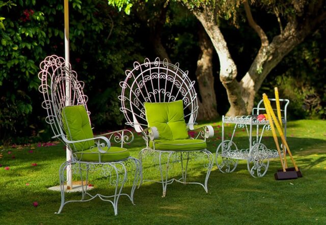 Two white metal chairs with green cushions on a lawn.
