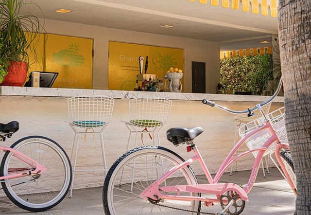 A pink bicycle parked in front of a white marble bar with yellow walls and white chairs.