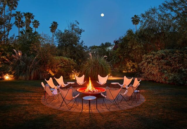 A fire pit with chairs around it in a grassy area at night with palm trees in the background.