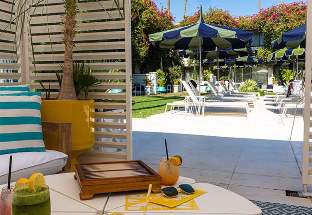 A poolside setting with a table, drinks, and lounge chairs under umbrellas.