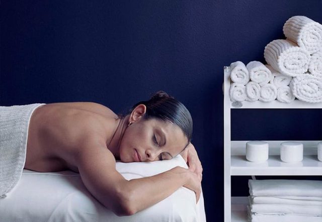 A woman lies on a massage table with a towel covering her body.