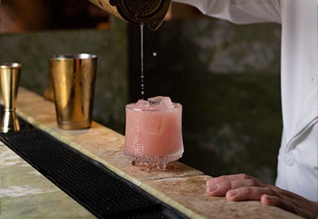 A bartender pouring a pink cocktail into a glass with ice.
