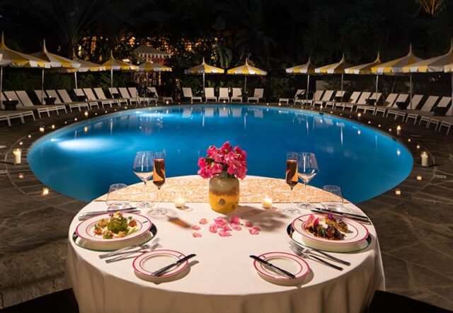 A romantic dinner setup by the pool at night with a beautiful view.