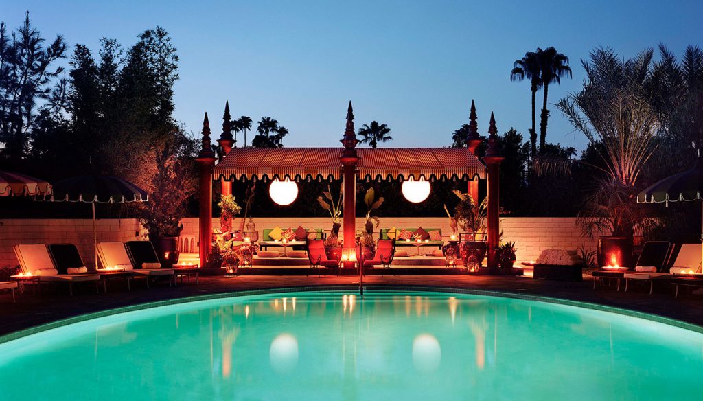 A serene poolside scene at dusk with a lit pool, lounge chairs, and a covered seating area.