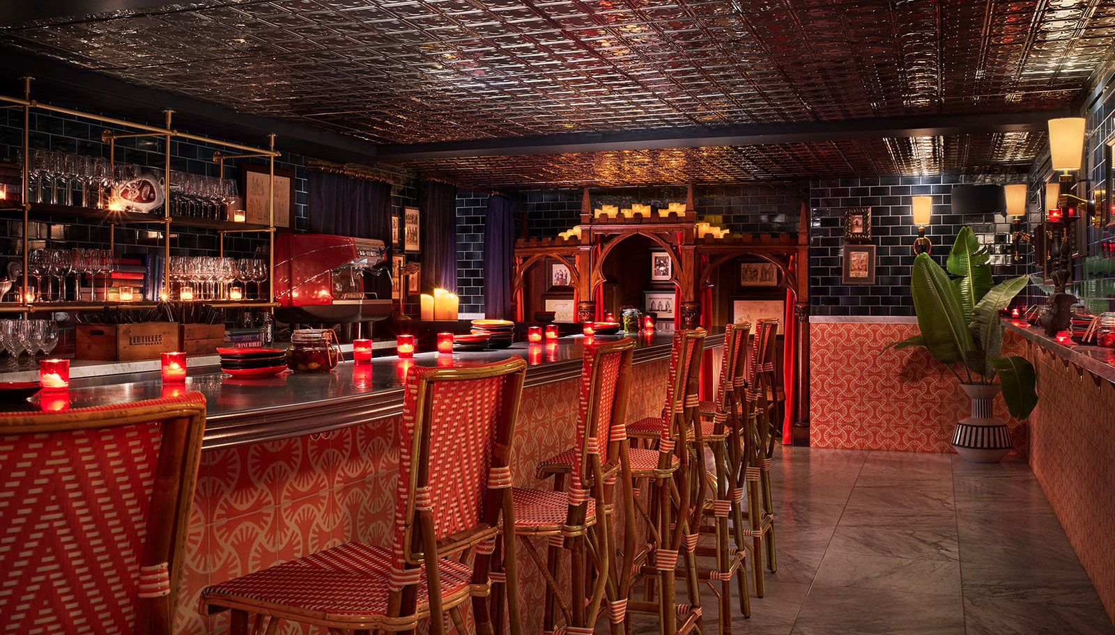 A dimly lit bar with red and gold chairs and candlelight.