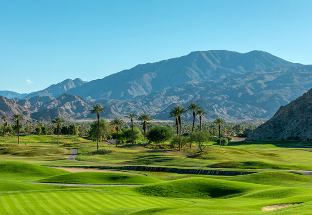 A wide view of a golf course with mountains in the background.
