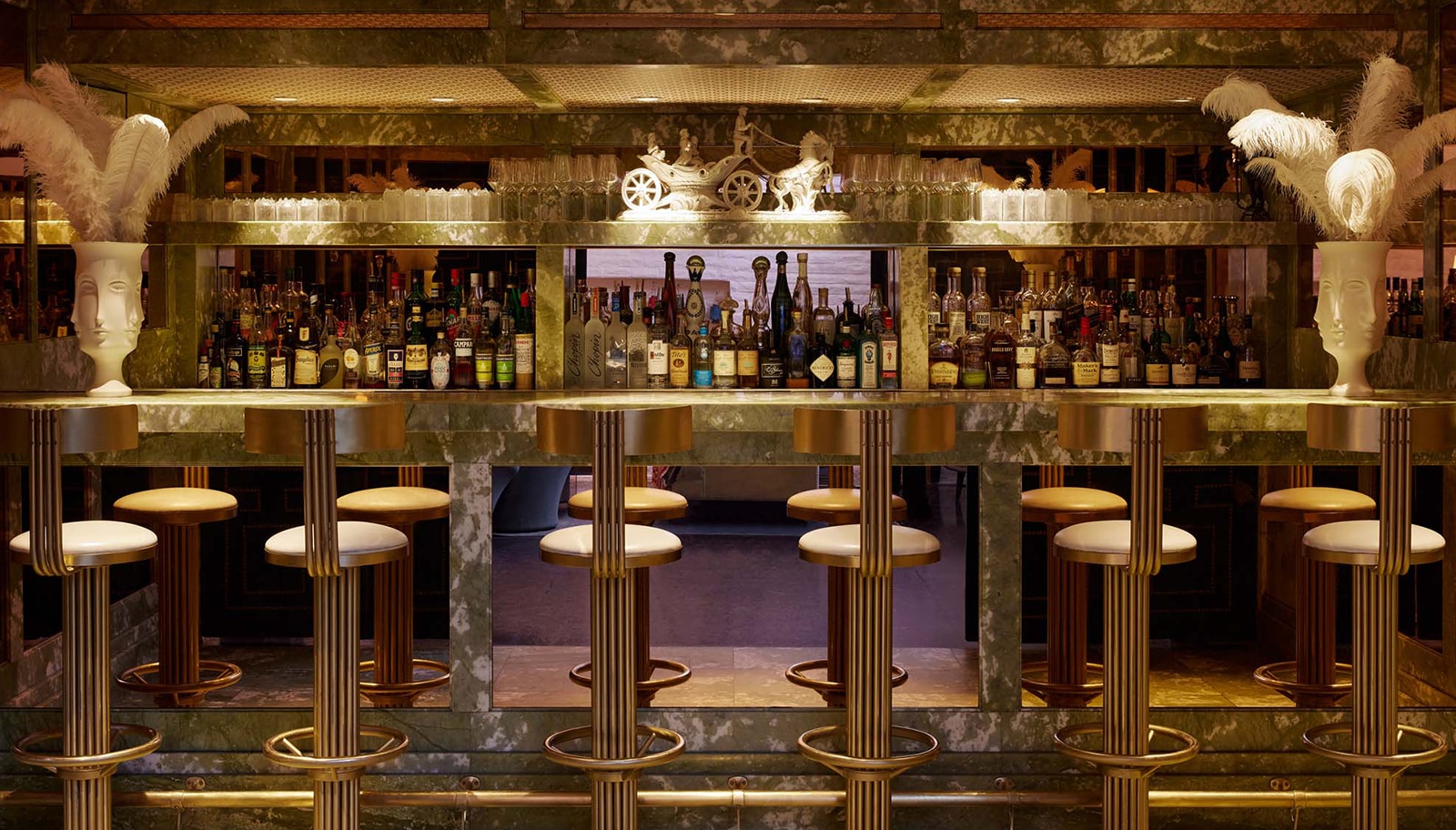 A luxurious bar with marble countertops, feathered decor, and numerous bottles of alcohol.