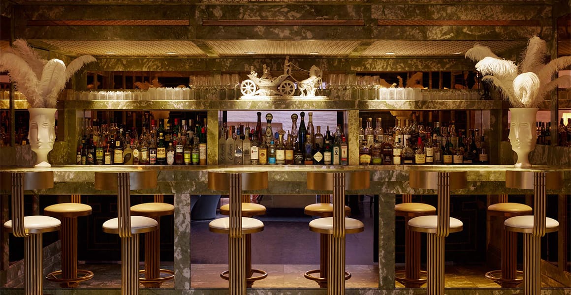 A wide view of a bar with stools, bottles, and marble countertops