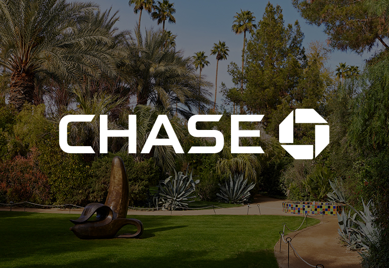 Large white CHASE logo and octagonal emblem centered over a lush garden with palm trees, sculptures, and greenery on a sunny day.