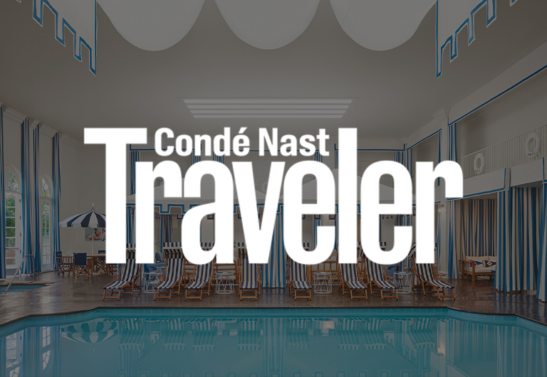 An indoor pool area with striped blue and white lounge chairs and curtains, overlaid with the Condé Nast Traveler logo in bold white letters.