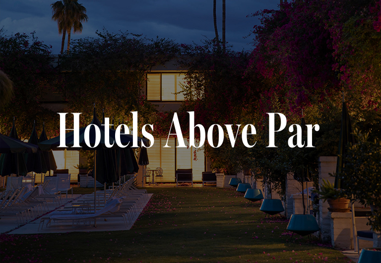 A hotel with glowing windows at dusk, surrounded by trees and empty lounge chairs, with the text Hotels Above Par centered over the image.