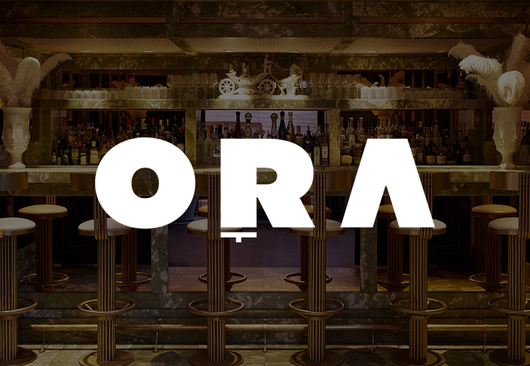 Bar with stools and shelves of liquor bottles in the background; large, bold white letters spelling ORA overlay the center of the image.