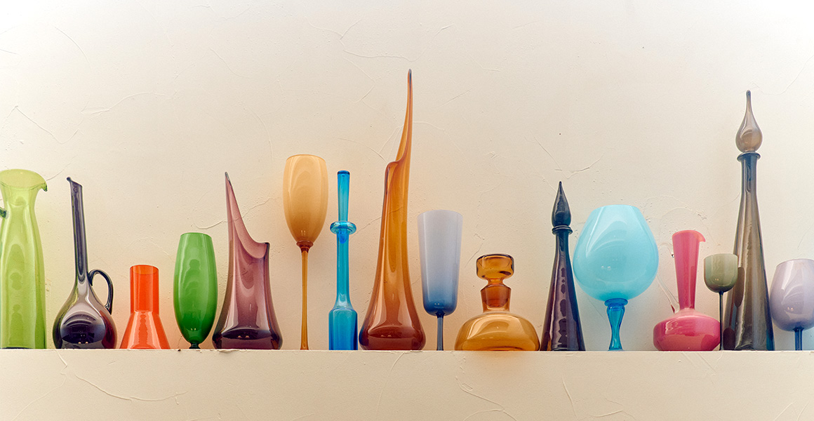 A collection of various colorful glass vases and decanters displayed on a shelf.