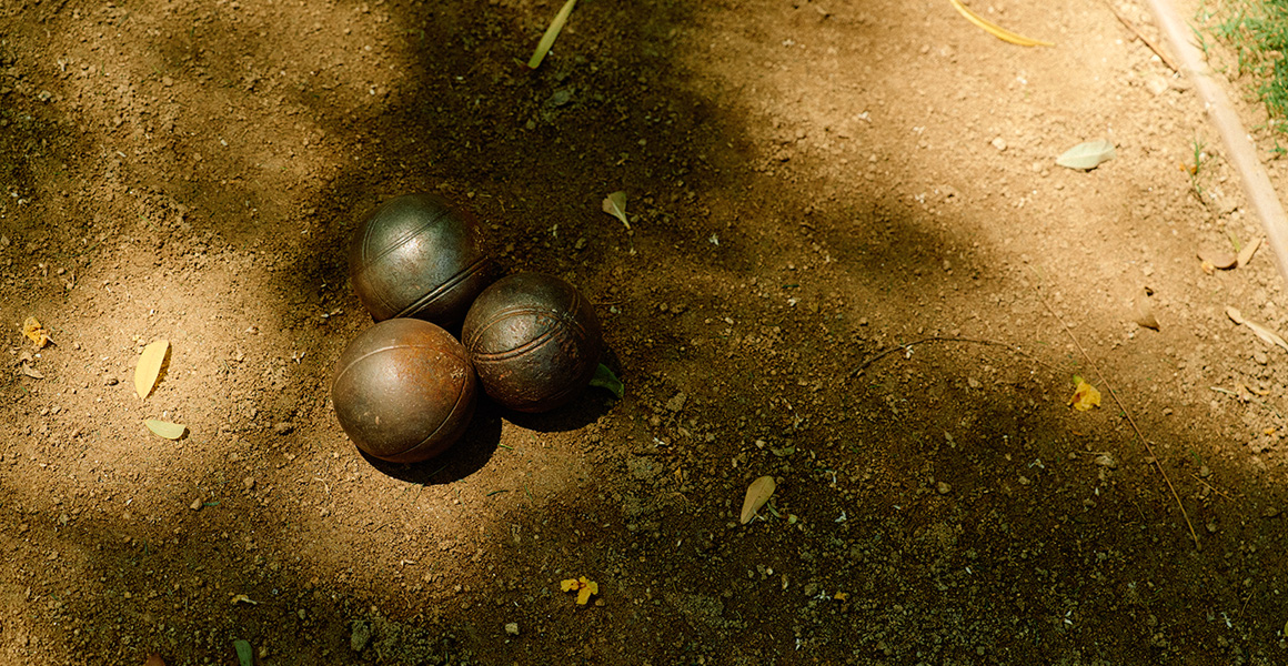 Three metal boules resting on a dirt court.