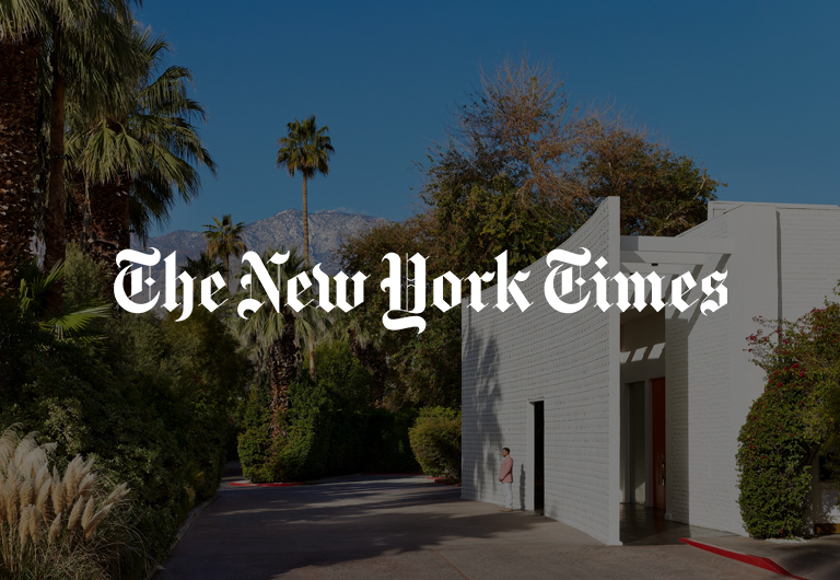 The New York Times logo overlaid on a photograph of a white modern building surrounded by palm trees and mountains.