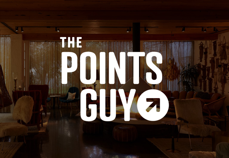 The Points Guy logo superimposed over a dimly lit, mid-century modern lounge with a central fireplace.